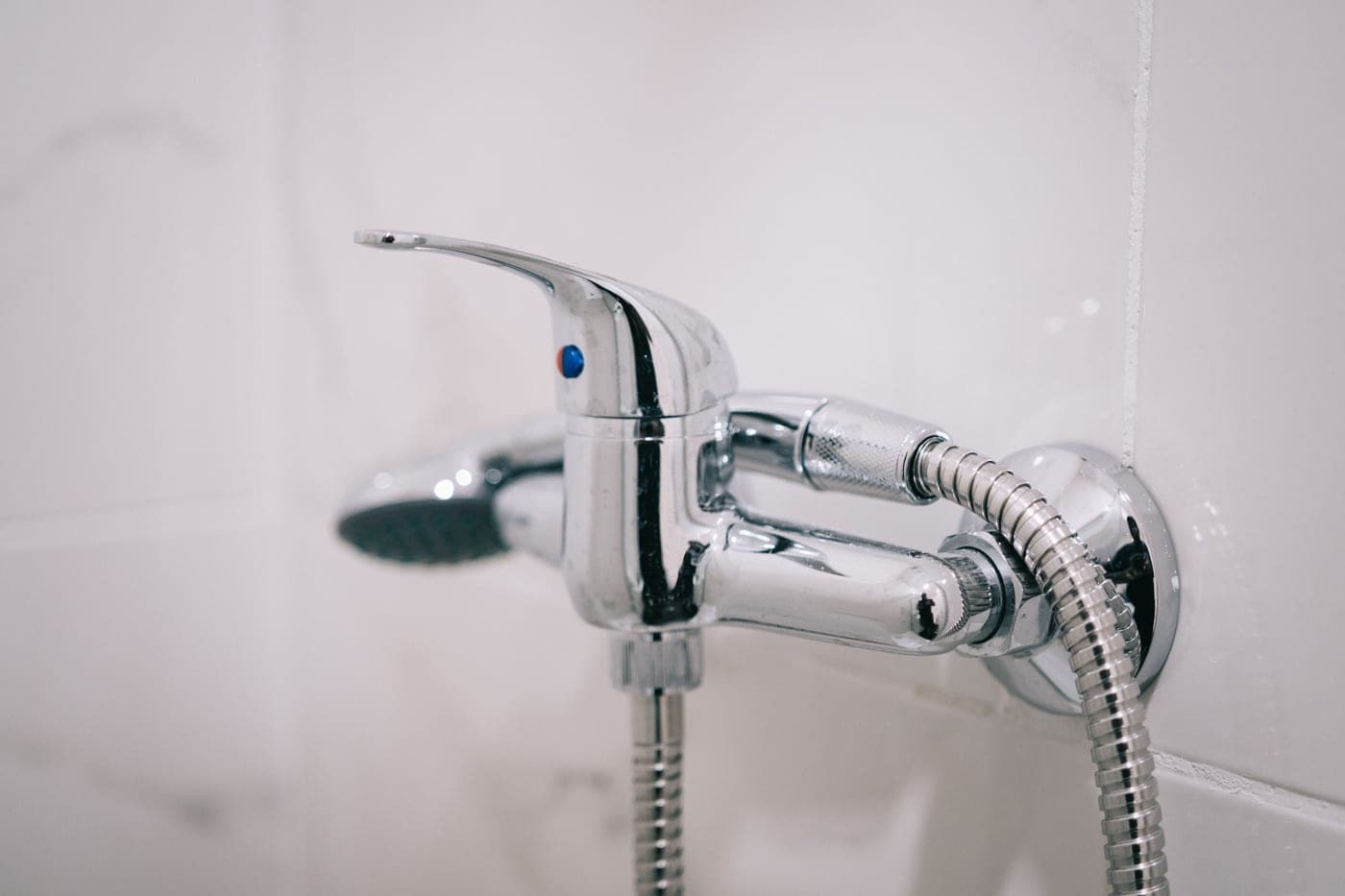A handheld shower wand and hose against a plain tiled wall
