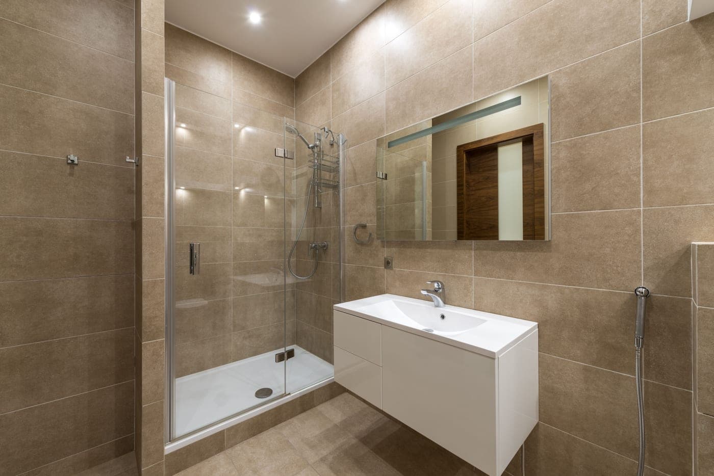 A wall-mounted shower head against plain tile, photographed straight on
