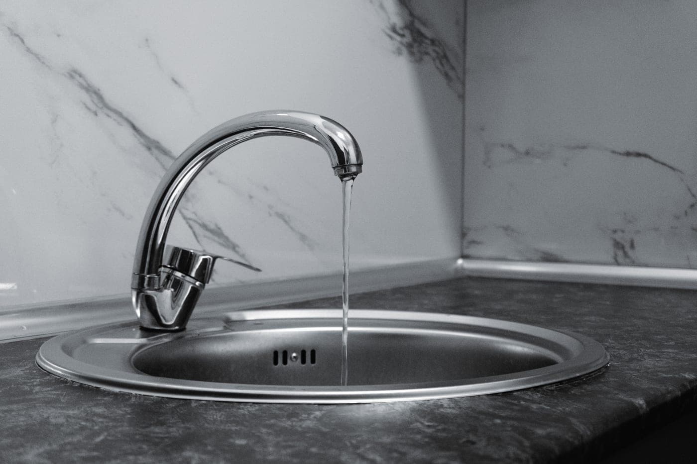 Water running from a chrome tap over a stainless steel surface